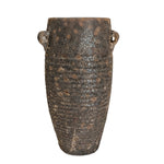 A rustic dark brown ceramic vase with a textured, speckled glaze and two small loop handles, displayed on a white pedestal against a neutral beige wall.